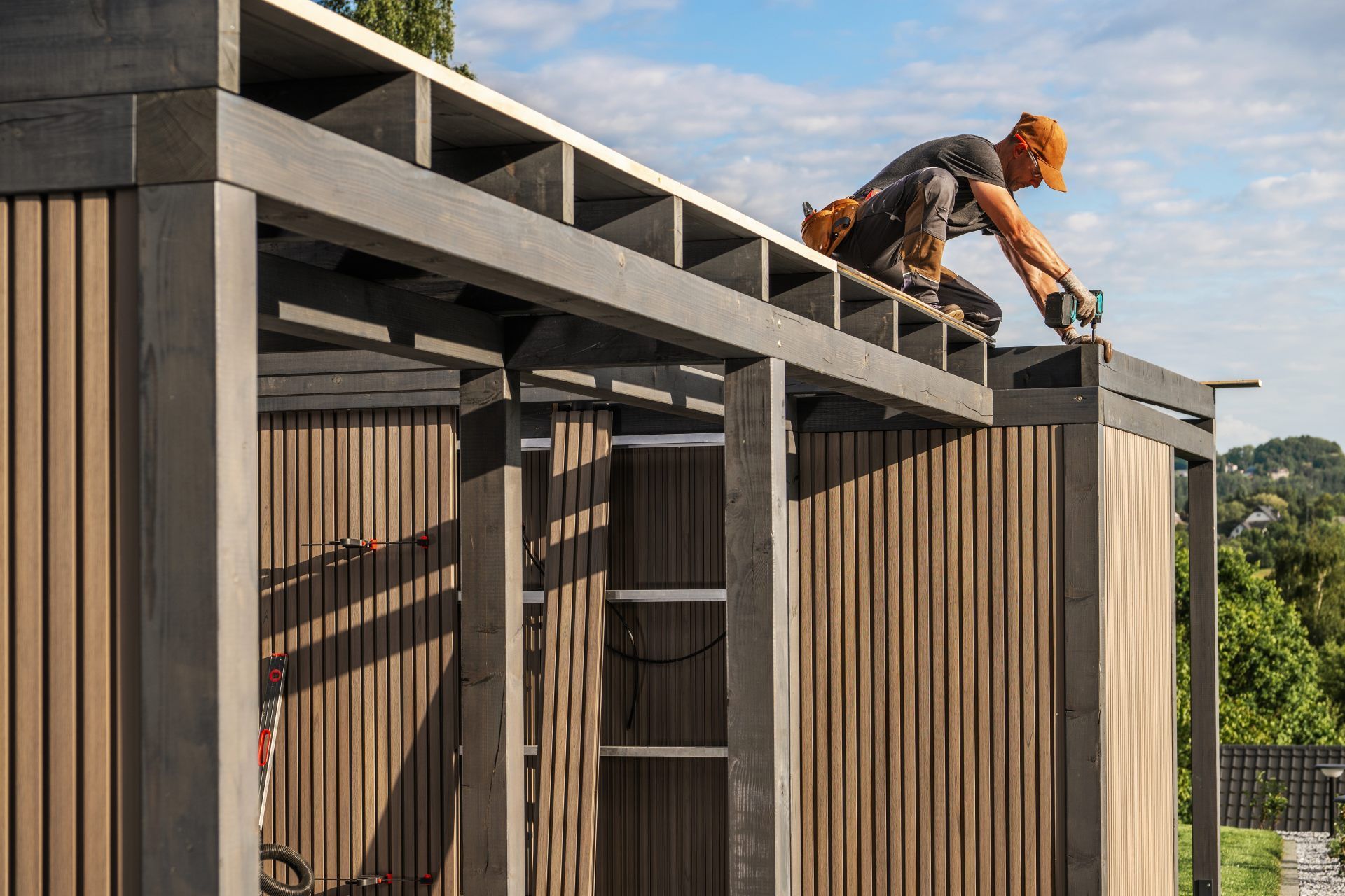 Construction worker on rooftop, building a wooden structure with vertical siding.