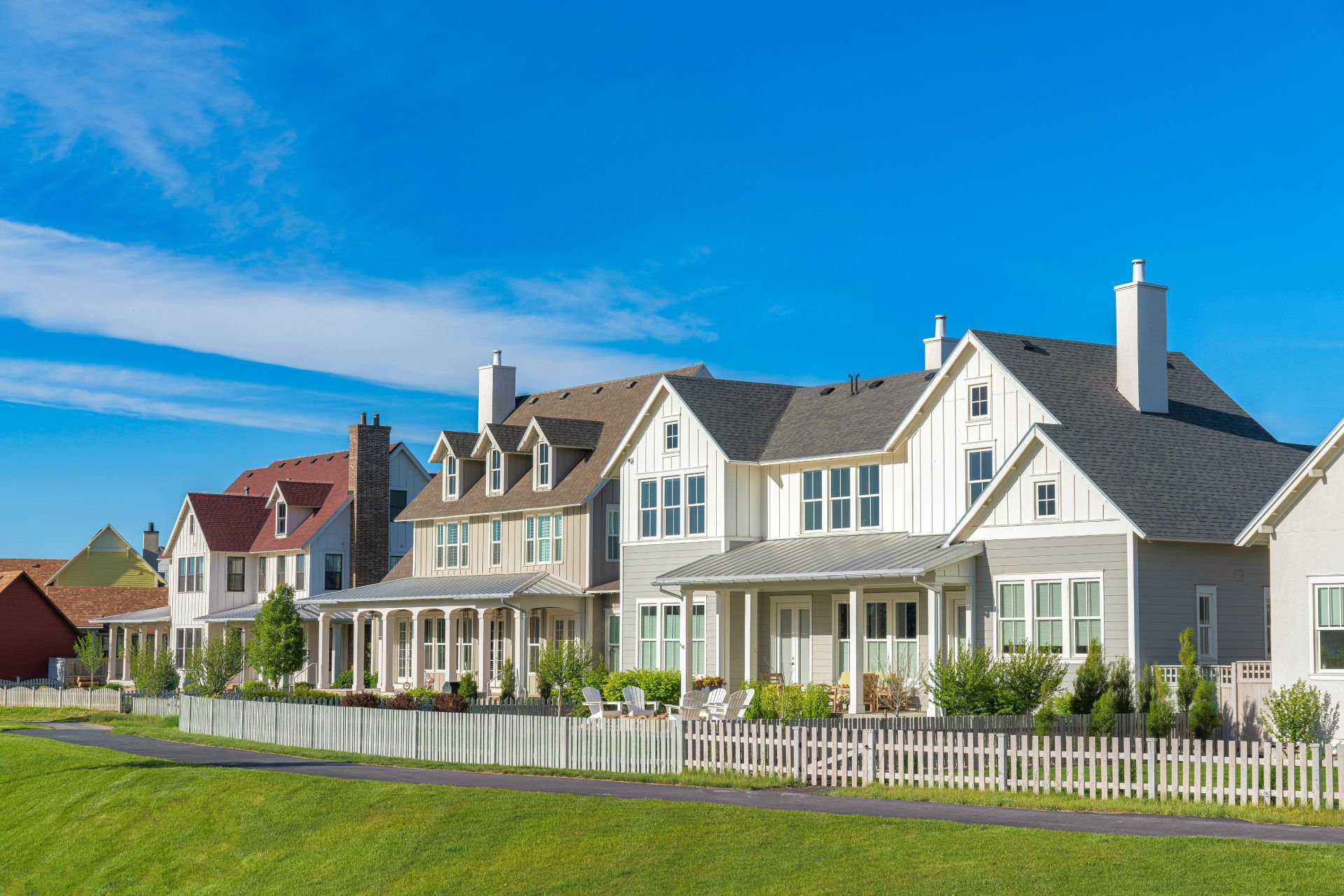 Row of modern houses with white picket fence and green lawn under a blue sky.