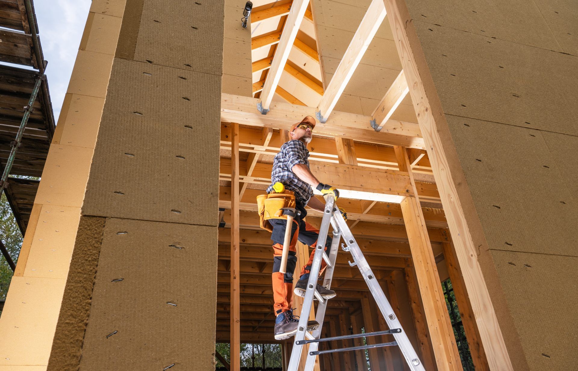 Construction worker on ladder, inside a building frame, installing insulation.