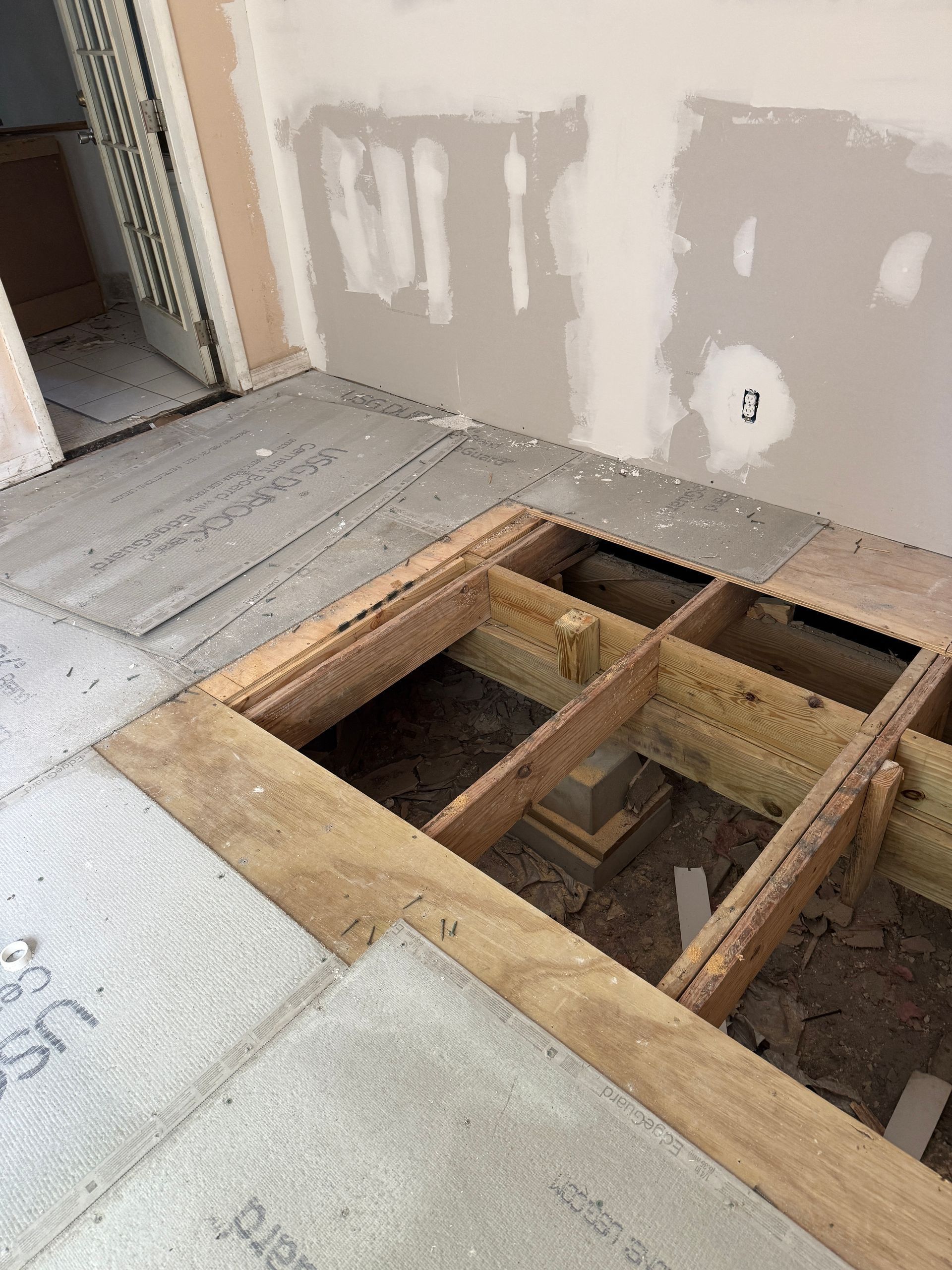 Wooden floor framing with some boards and a section cut out, ready for tile installation.