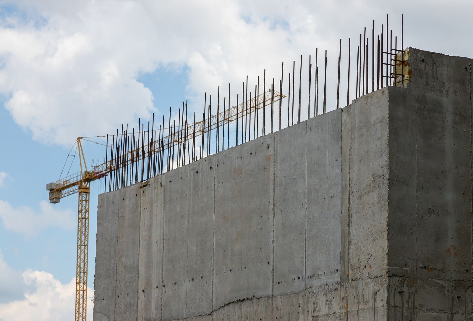 Construction site with a concrete wall, rebar, and a crane against a cloudy sky.