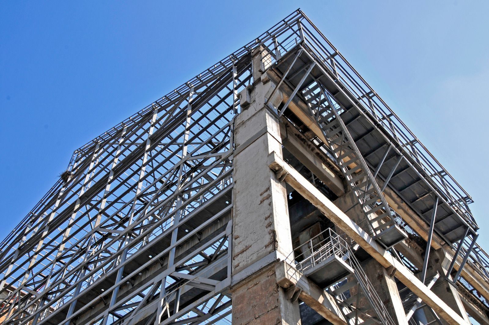 Steel frame of a tall building under construction, against a clear blue sky.