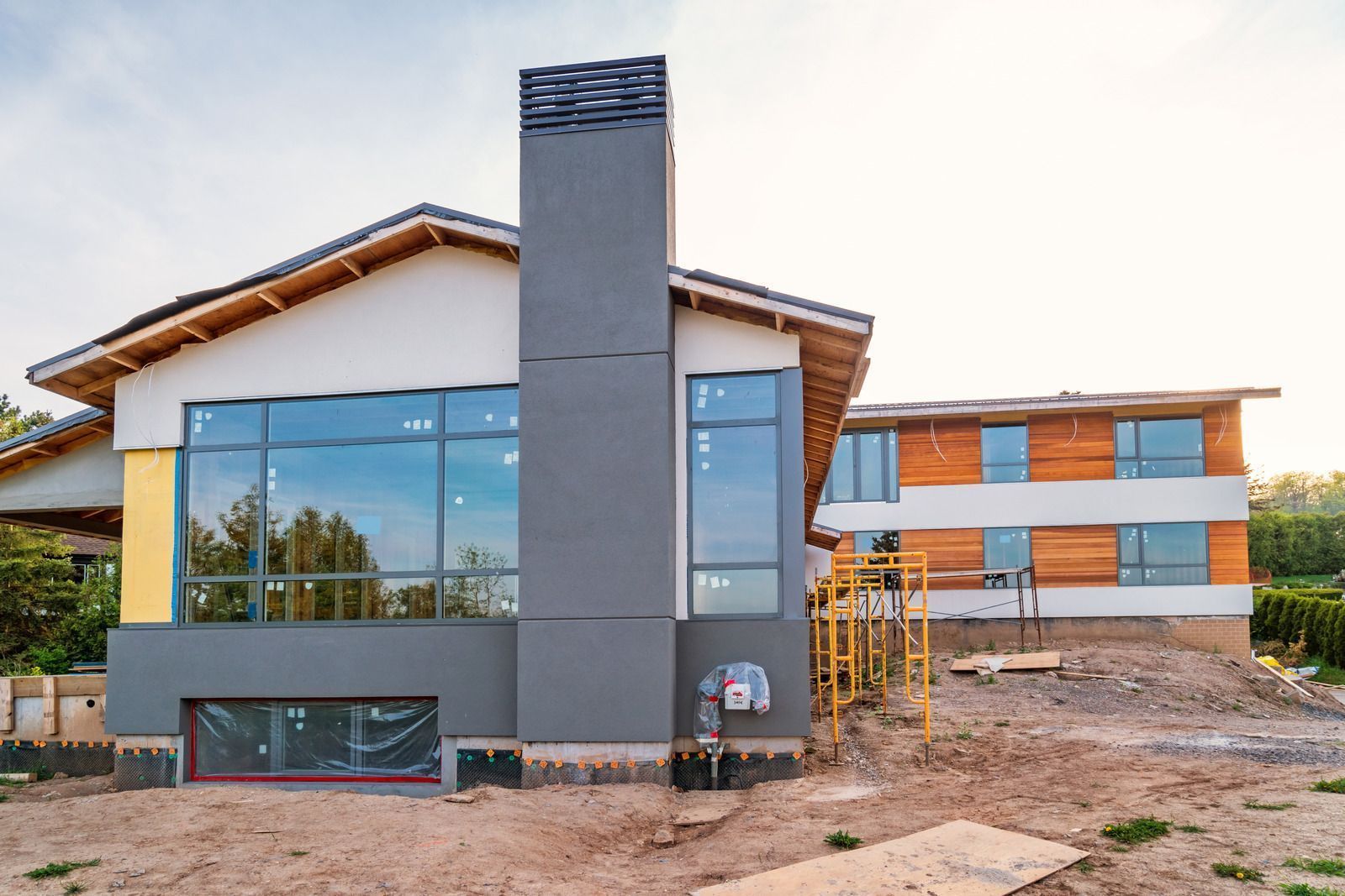 Modern house under construction with large windows and a tall chimney.
