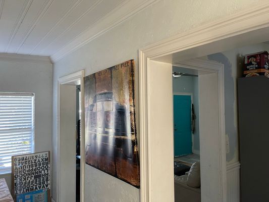 Hallway with artwork on the wall, leading to rooms with teal and white painted doors.