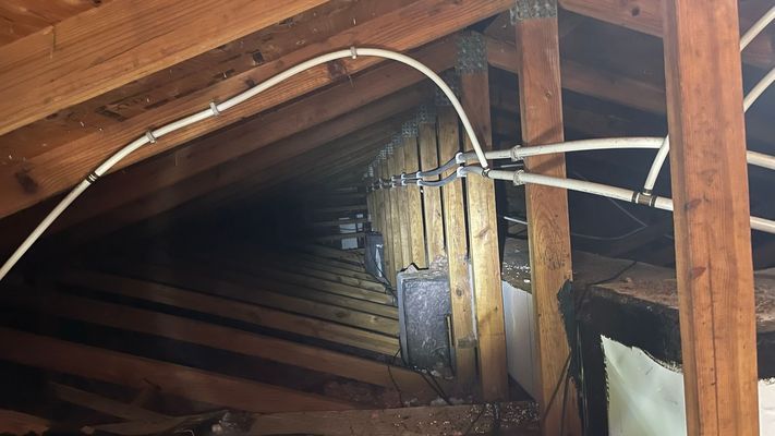 Attic space with wooden beams and white conduit. Dark interior, angled perspective.