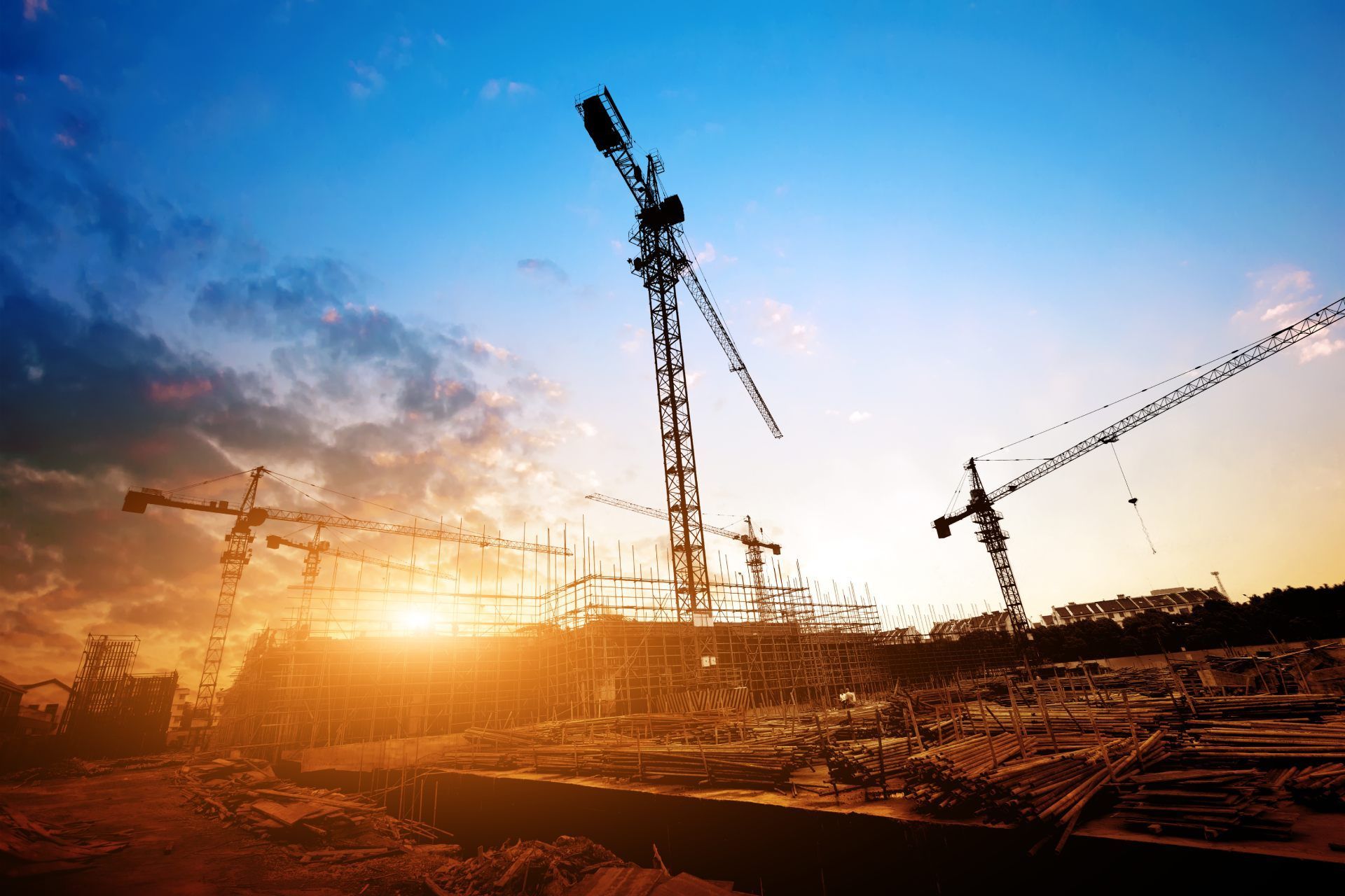 Construction site with cranes silhouetted against a sunset.