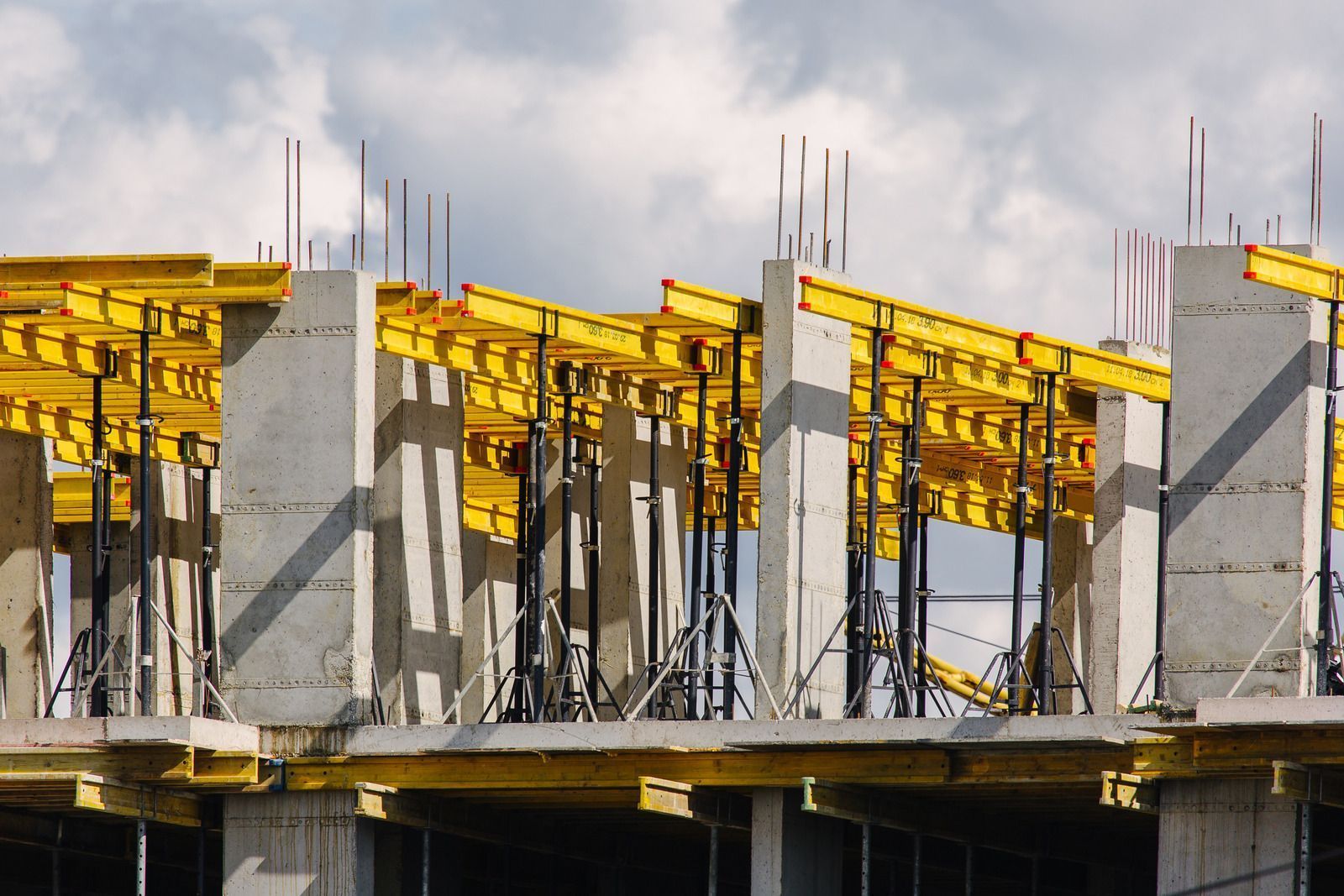 Construction site with concrete columns and yellow scaffolding supporting a partially constructed floor.