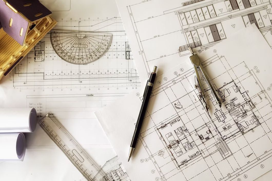 Architectural blueprints with tools and miniature house model on a white surface.