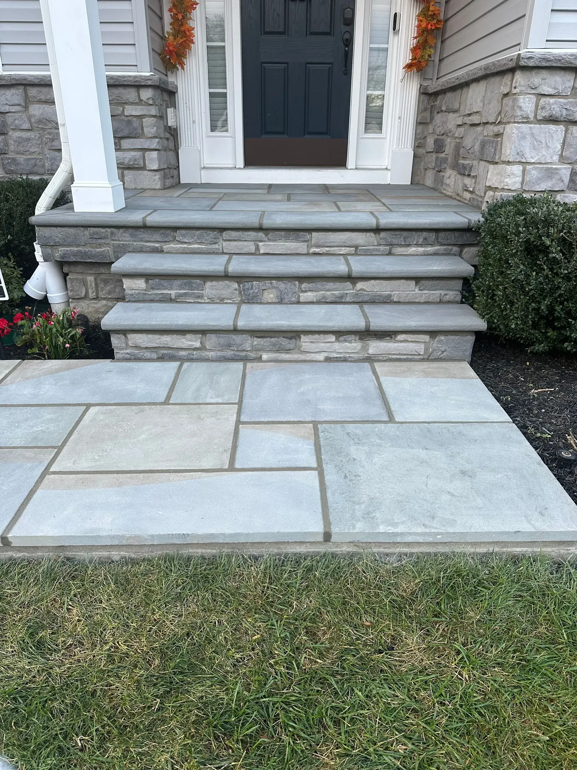 Front entrance with stone steps leading to a gray door and a paved walkway across the lawn. Front entrance with stone steps leading to a gray door and a paved walkway across the lawn.