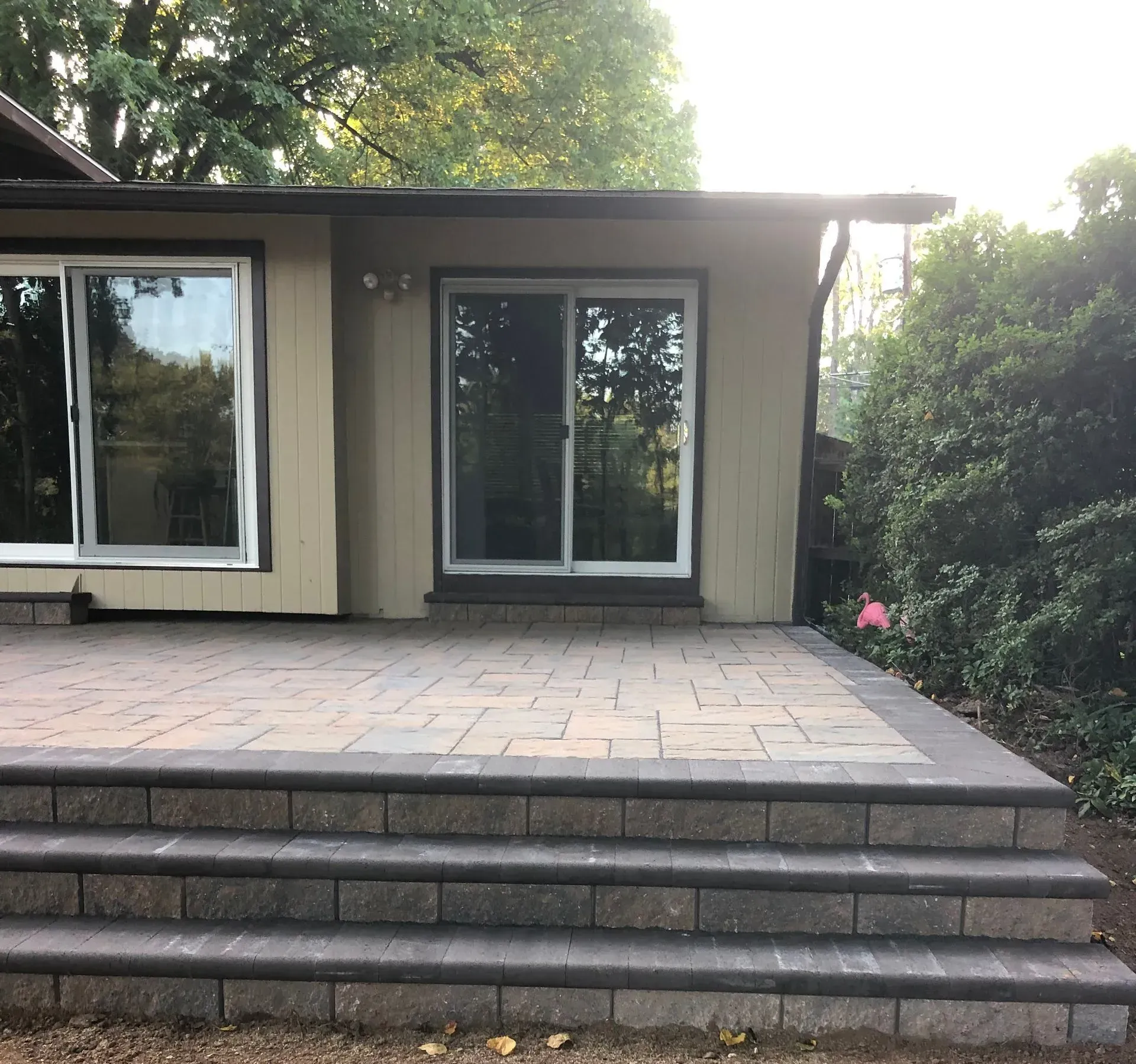 Back patio with stone steps leading to a beige house with sliding glass doors and surrounding trees. Back patio with stone steps leading to a beige house with sliding glass doors and surrounding trees.