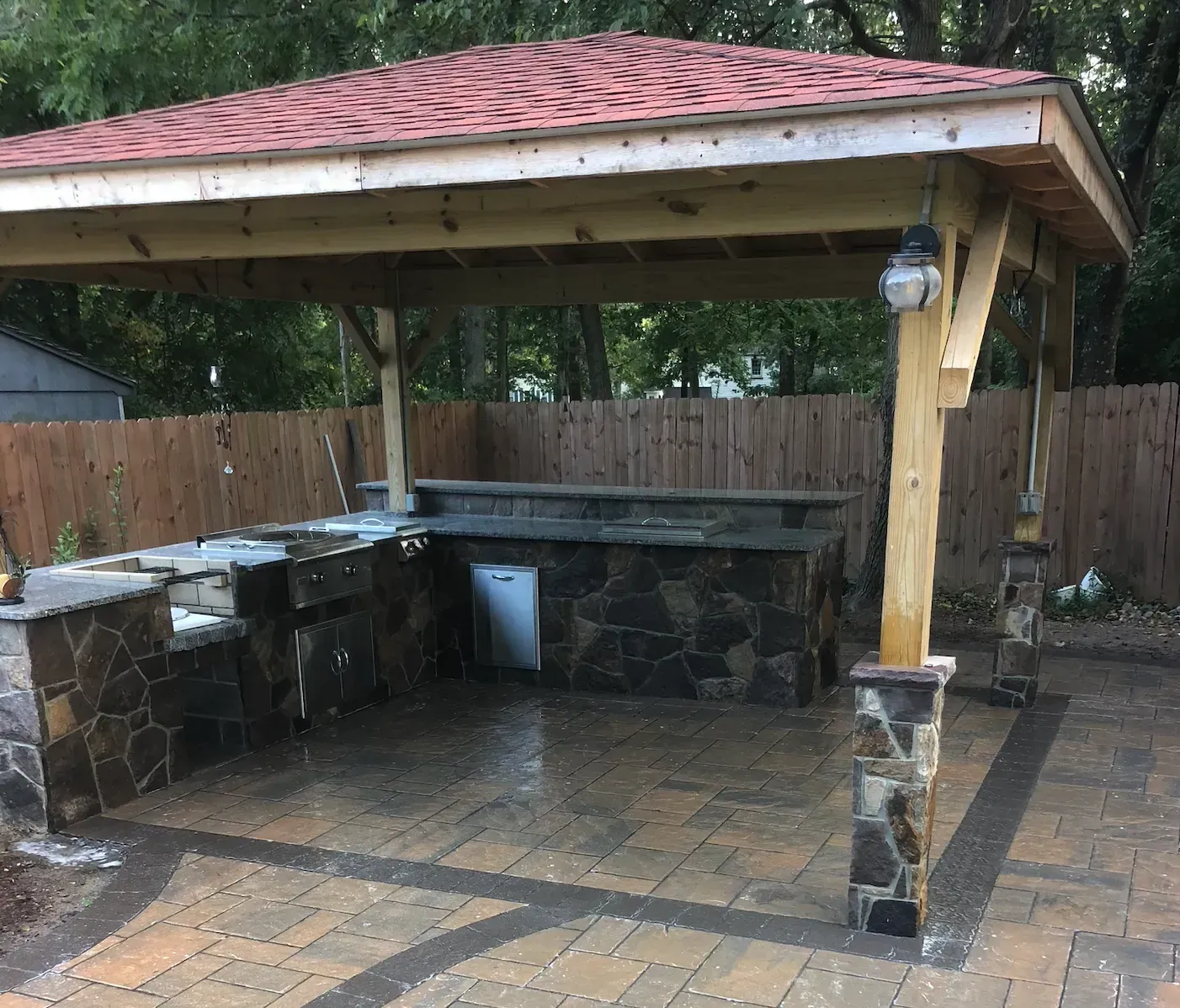 Covered outdoor stone bar with wooden posts and a red roof in a backyard patio. Covered outdoor stone bar with wooden posts and a red roof in a backyard patio.