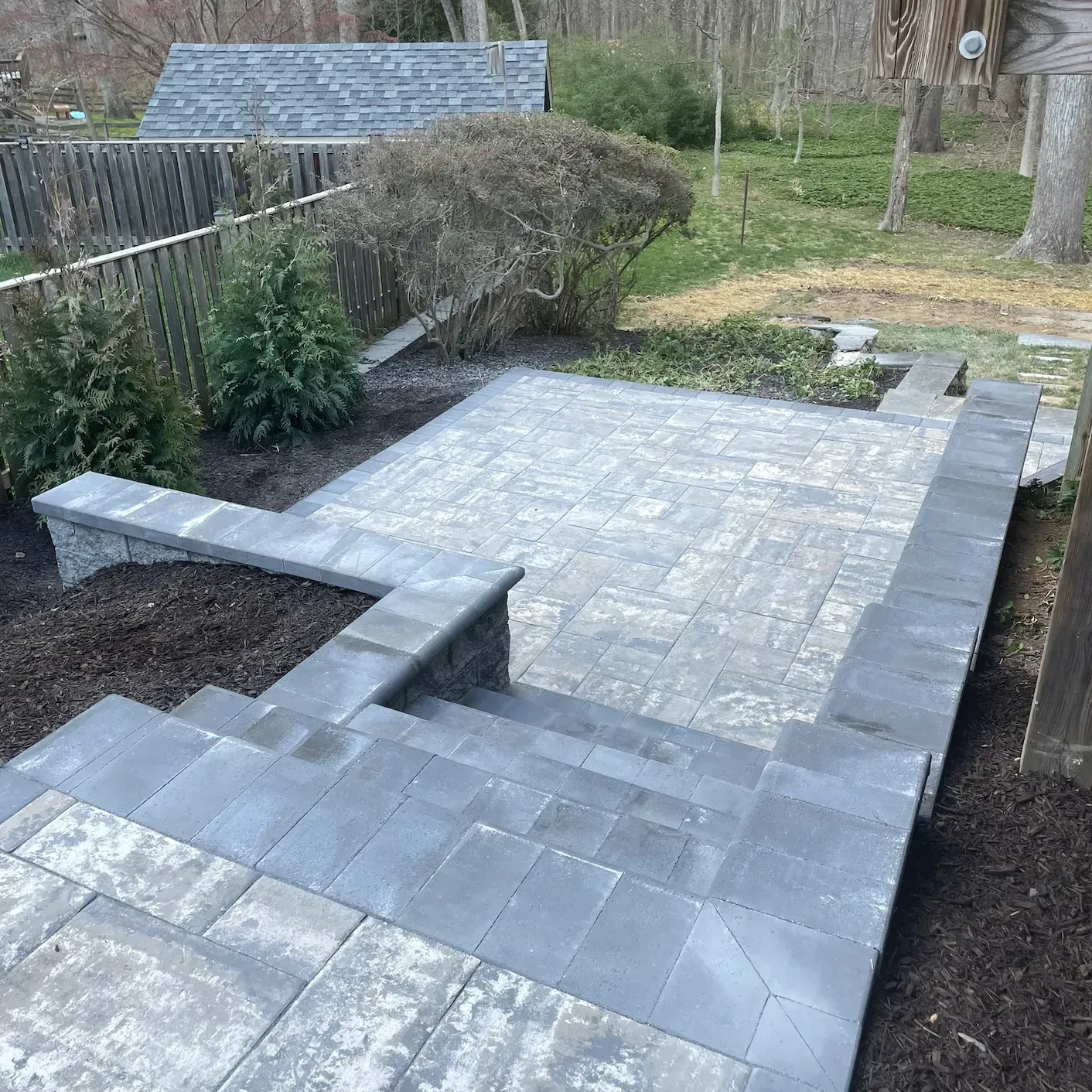 Newly paved gray stone patio with steps in a backyard garden