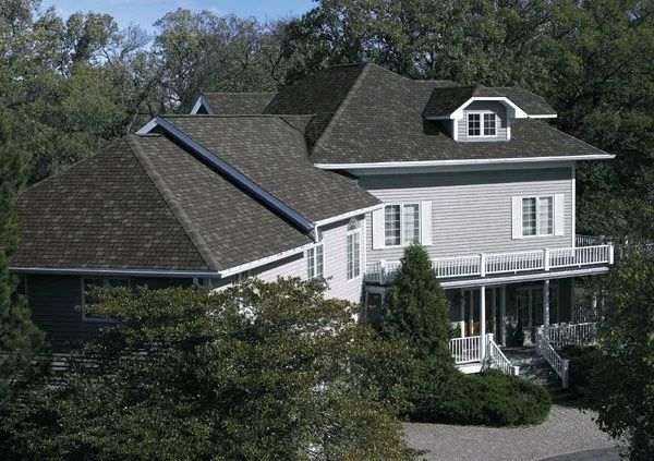 A large white house with a gray roof is surrounded by trees