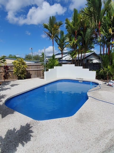 Backyard swimming pool with blue water, white deck, and tropical plants under a sunny sky