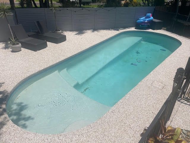 Backyard swimming pool with clear water, white gravel deck, lounge chairs, and an inflatable float