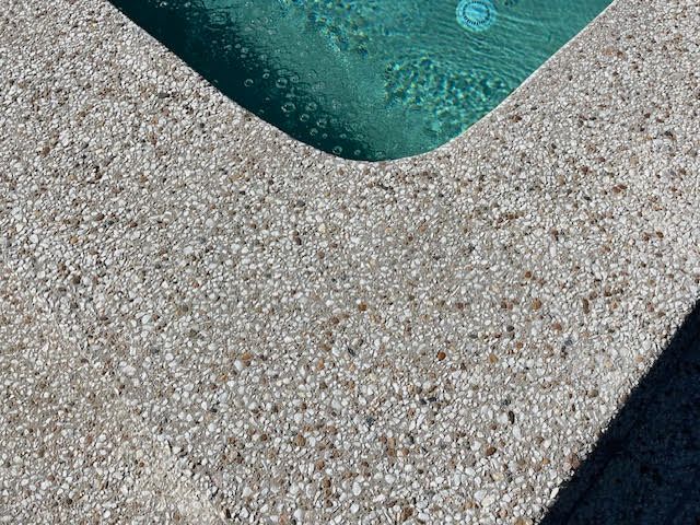 Teal pool water beside a textured beige concrete pool deck