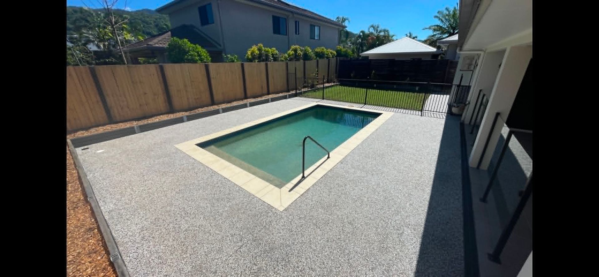 Backyard with a small in-ground pool, gravel patio, and wooden fence under a sunny sky
