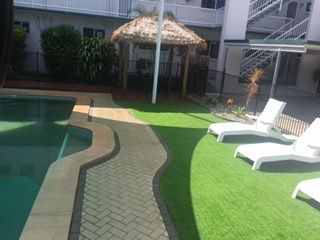 Poolside paving curved around the pool with new artificial turf and a thatched umbrella installed