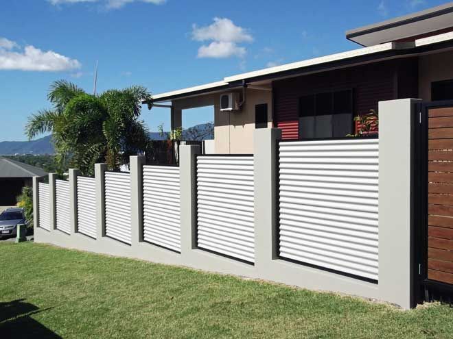 Modern house with white louvered fence panels and a brick pillar along a grassy street.