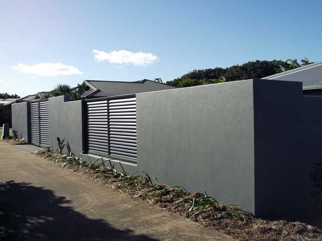 Gray concrete wall and metal gates lining a street under a bright blue sky