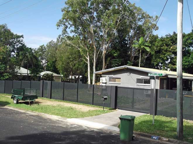 Residential house with gray fence, green bins, and trees along a quiet street