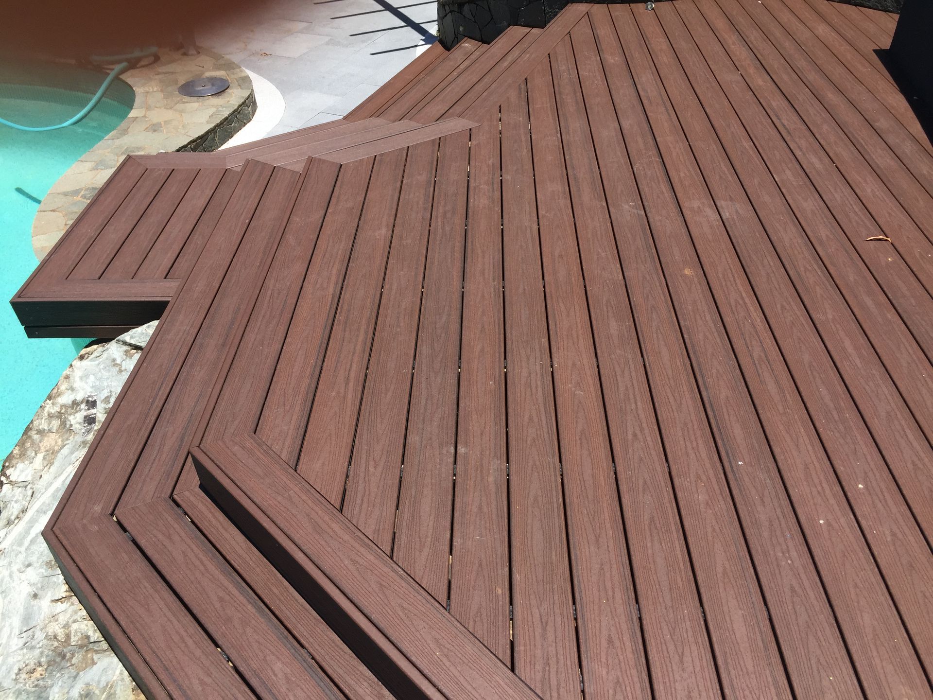 Tiered composite decking raised patio area beside pool installed