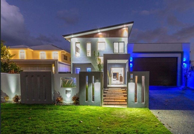 Modern two-story house at dusk with lit windows, front steps, and blue accent lighting by the garage.