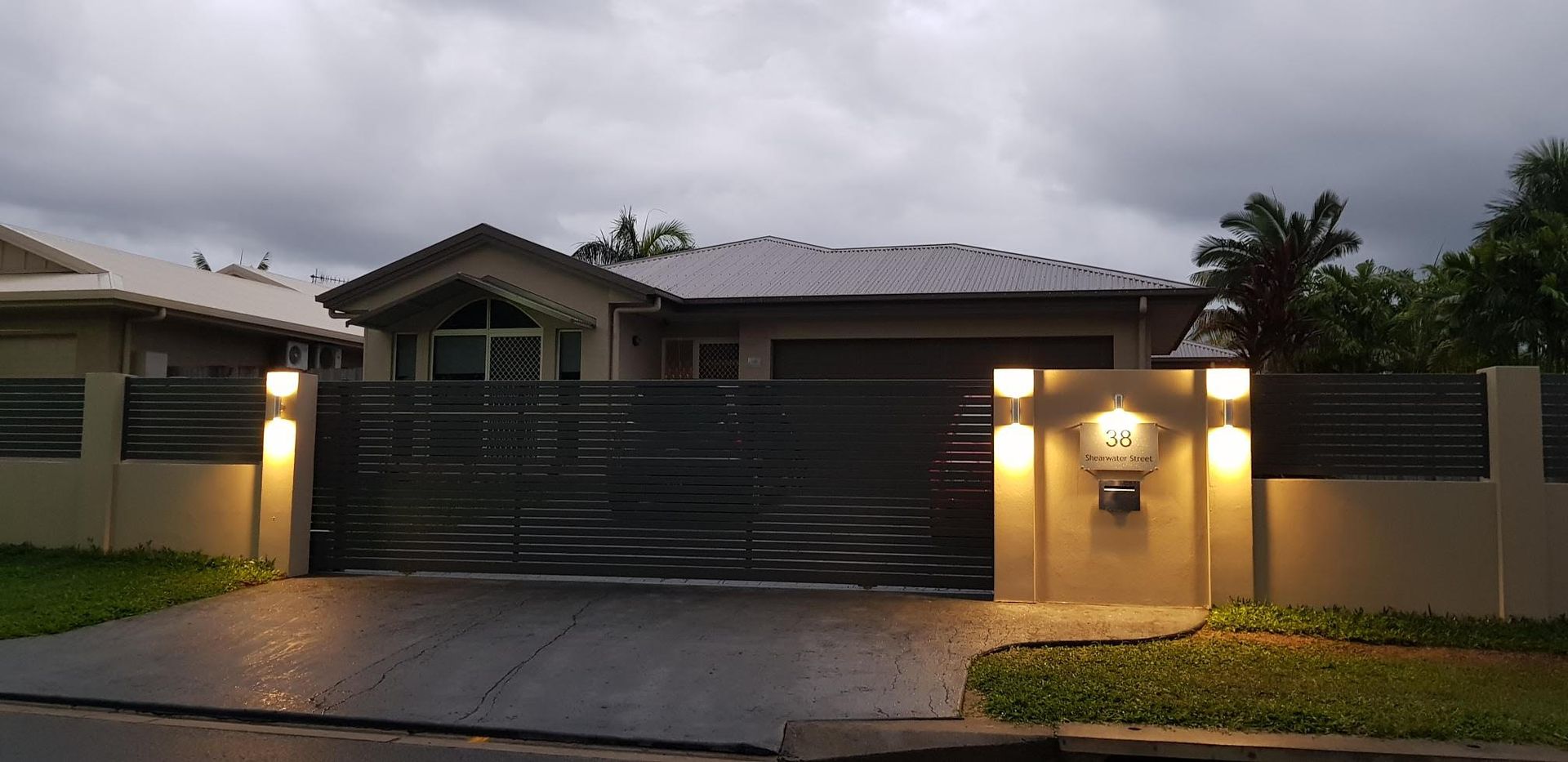 Modern single-story house with a dark gate and warm exterior lights at dusk