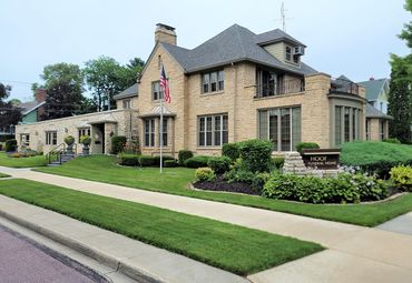Stone church with a steep roof, manicured lawn, and sidewalk beside a street.