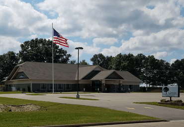 Single-story building with an American flag, parking lot, and cloudy sky.
