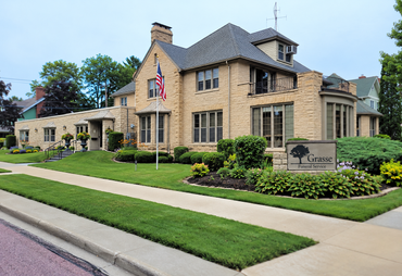 Stone apartment building with manicured lawn, sidewalk, and a sign at the entrance