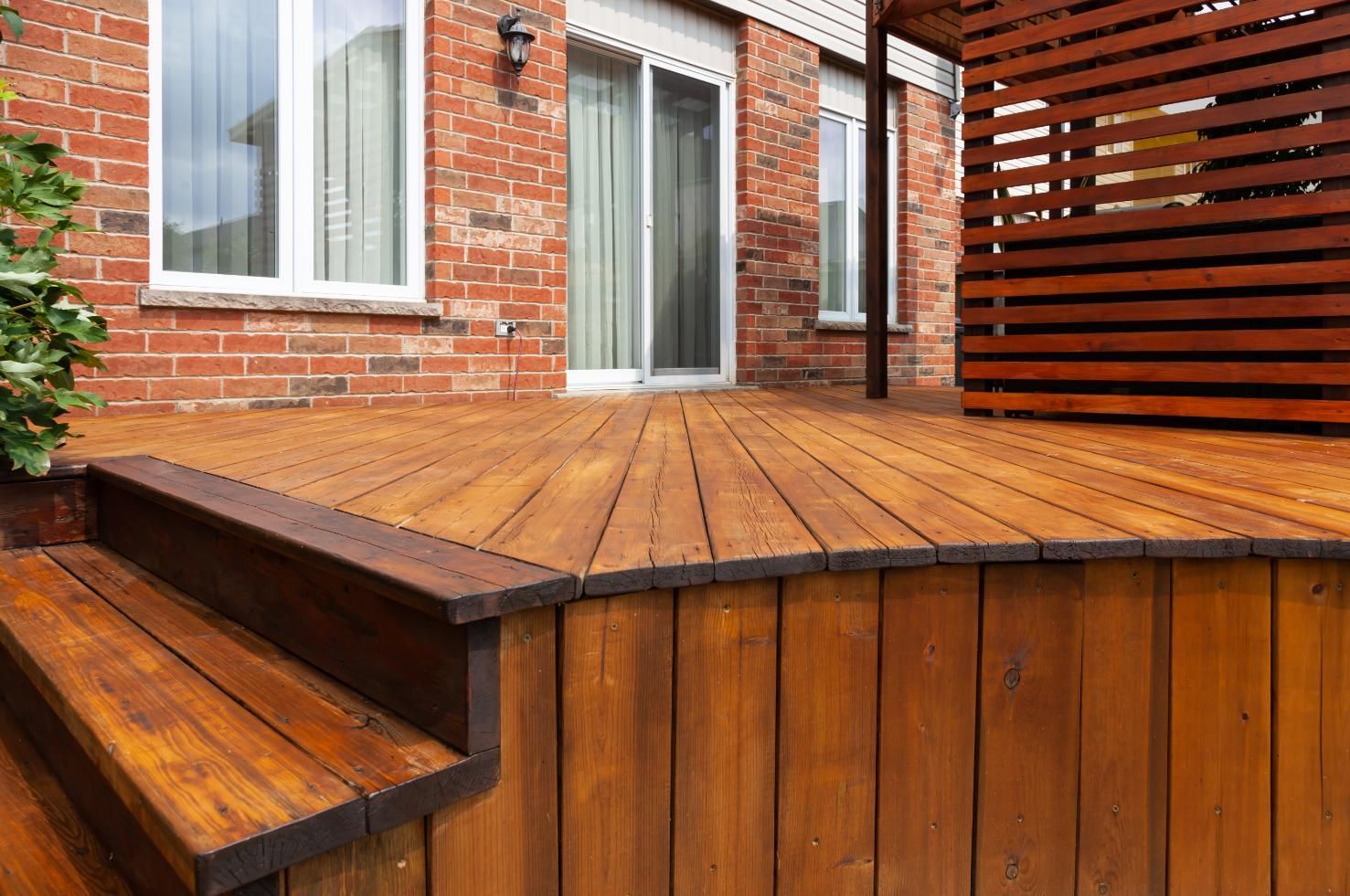 A wooden deck with stairs leading up to it in front of a brick house.
