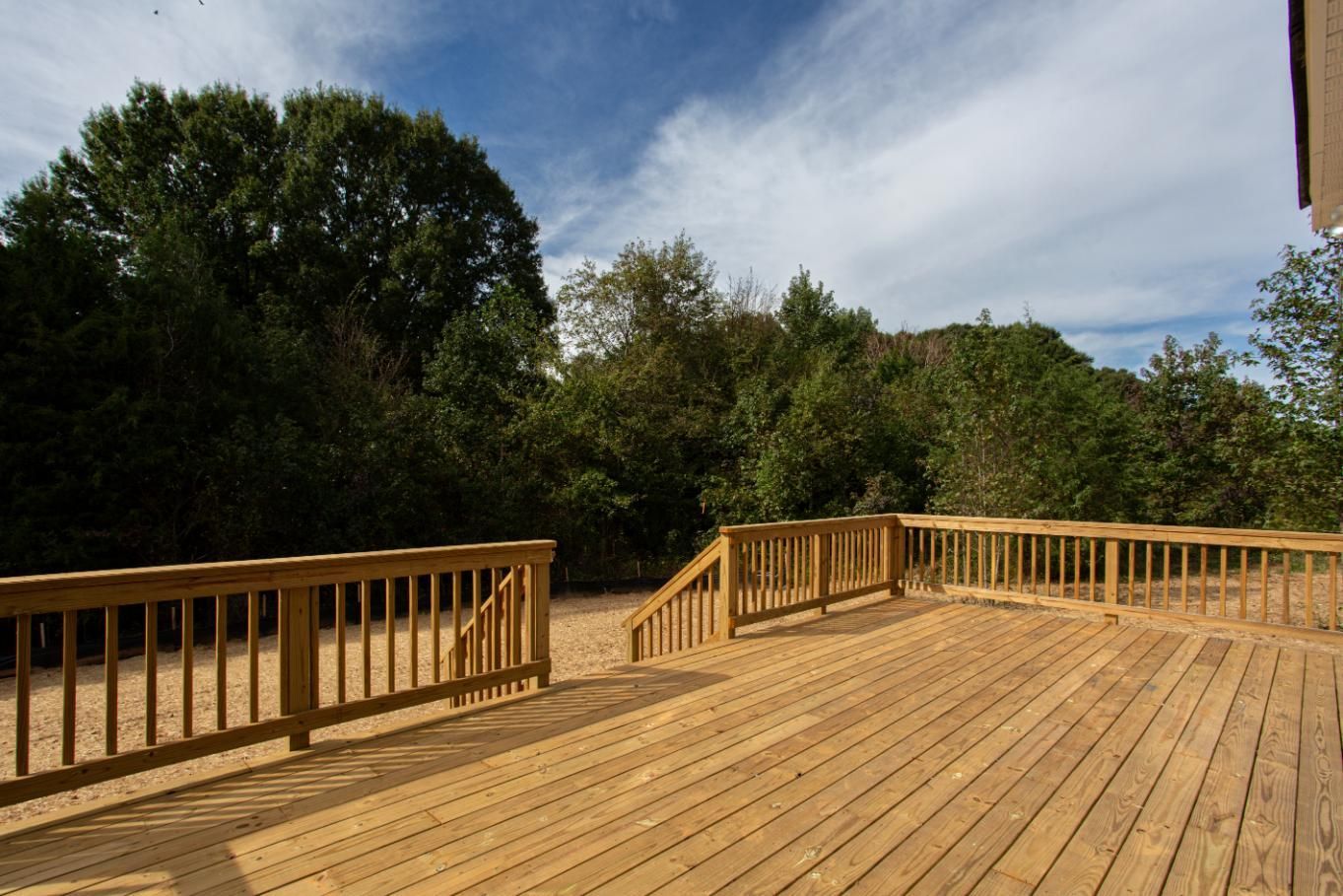 A large wooden deck with stairs leading up to it and trees in the background.