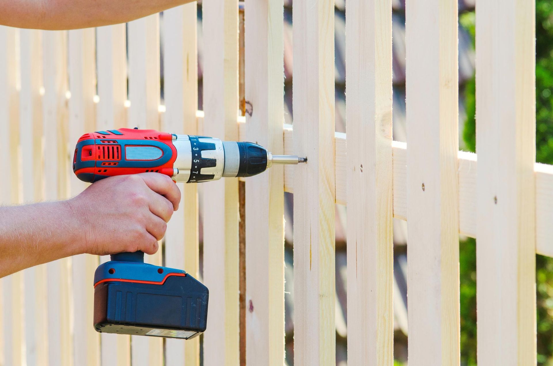 A man is using a drill to fix a wooden fence.