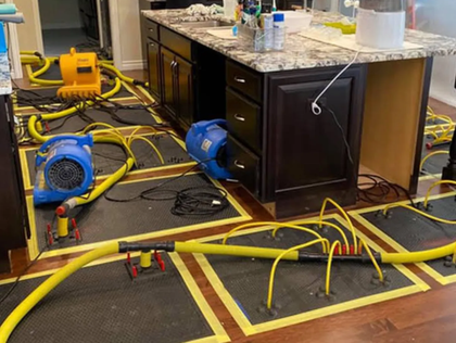 Messy workshop floor with blue fans, yellow hoses, and a cabinet under a granite countertop