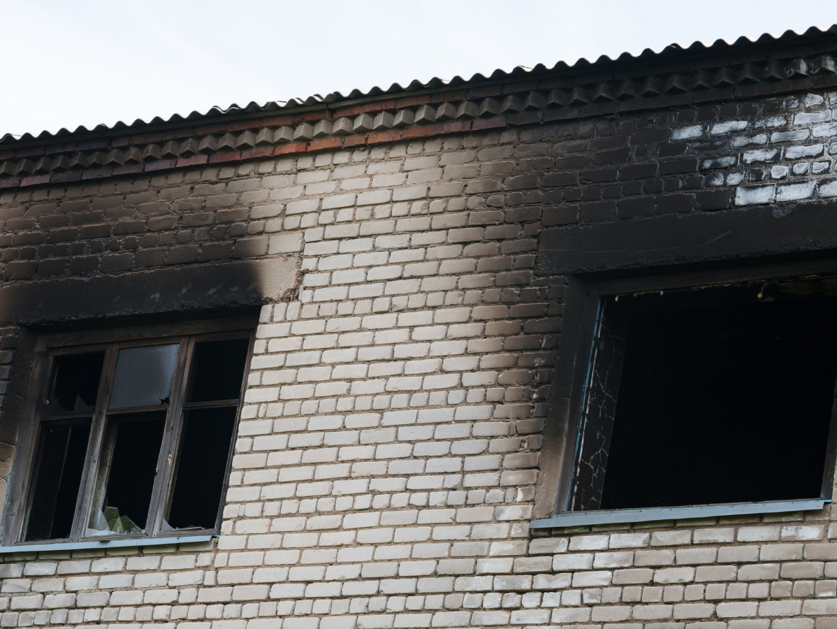 Soot-blackened brick building façade with two open, fire-damaged windows