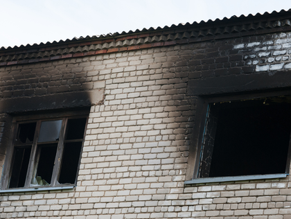 Soot-blackened brick building façade with two open, fire-damaged windows