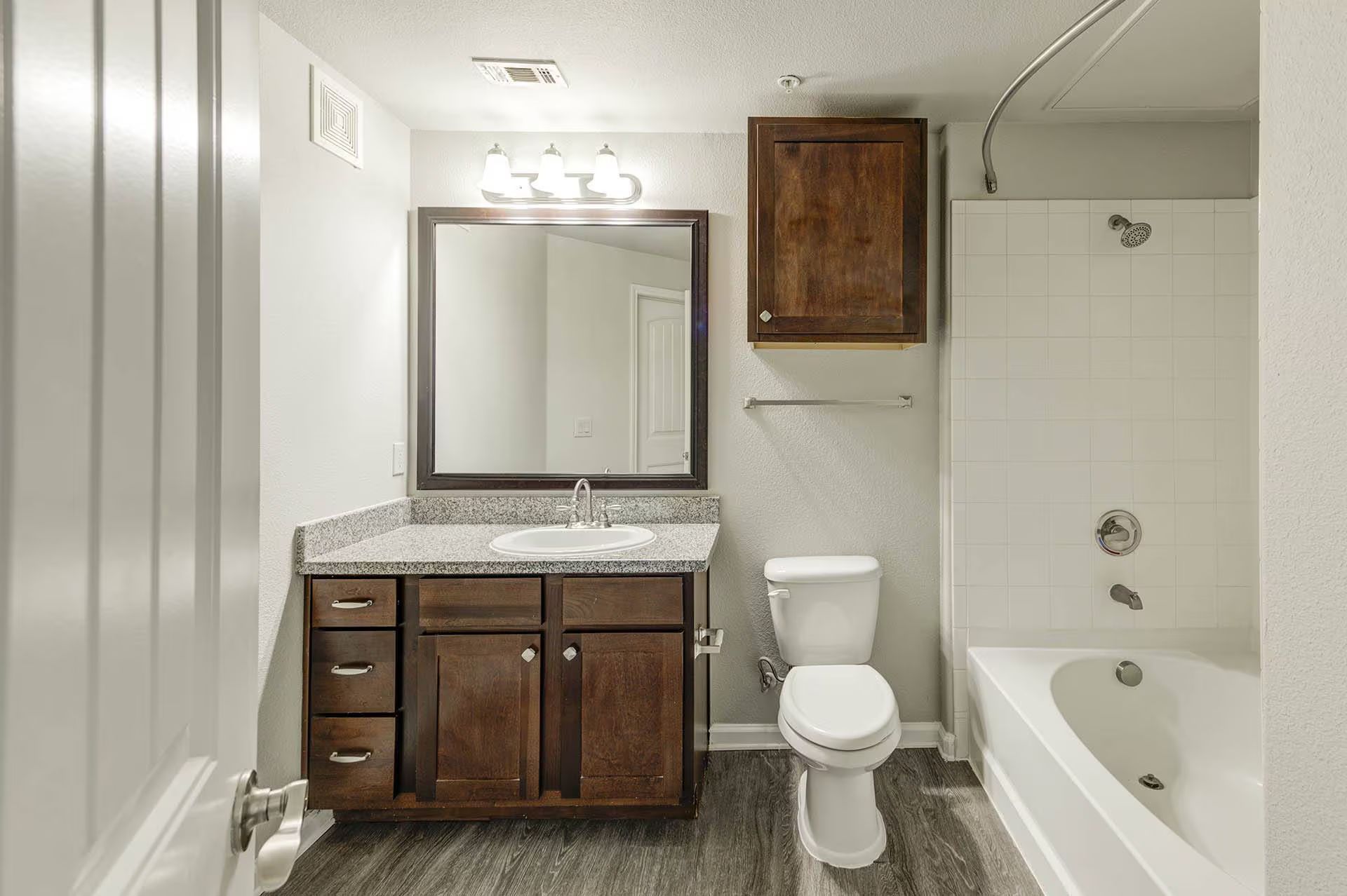 Bathroom with dark wood vanity, granite countertop, and white bathtub.