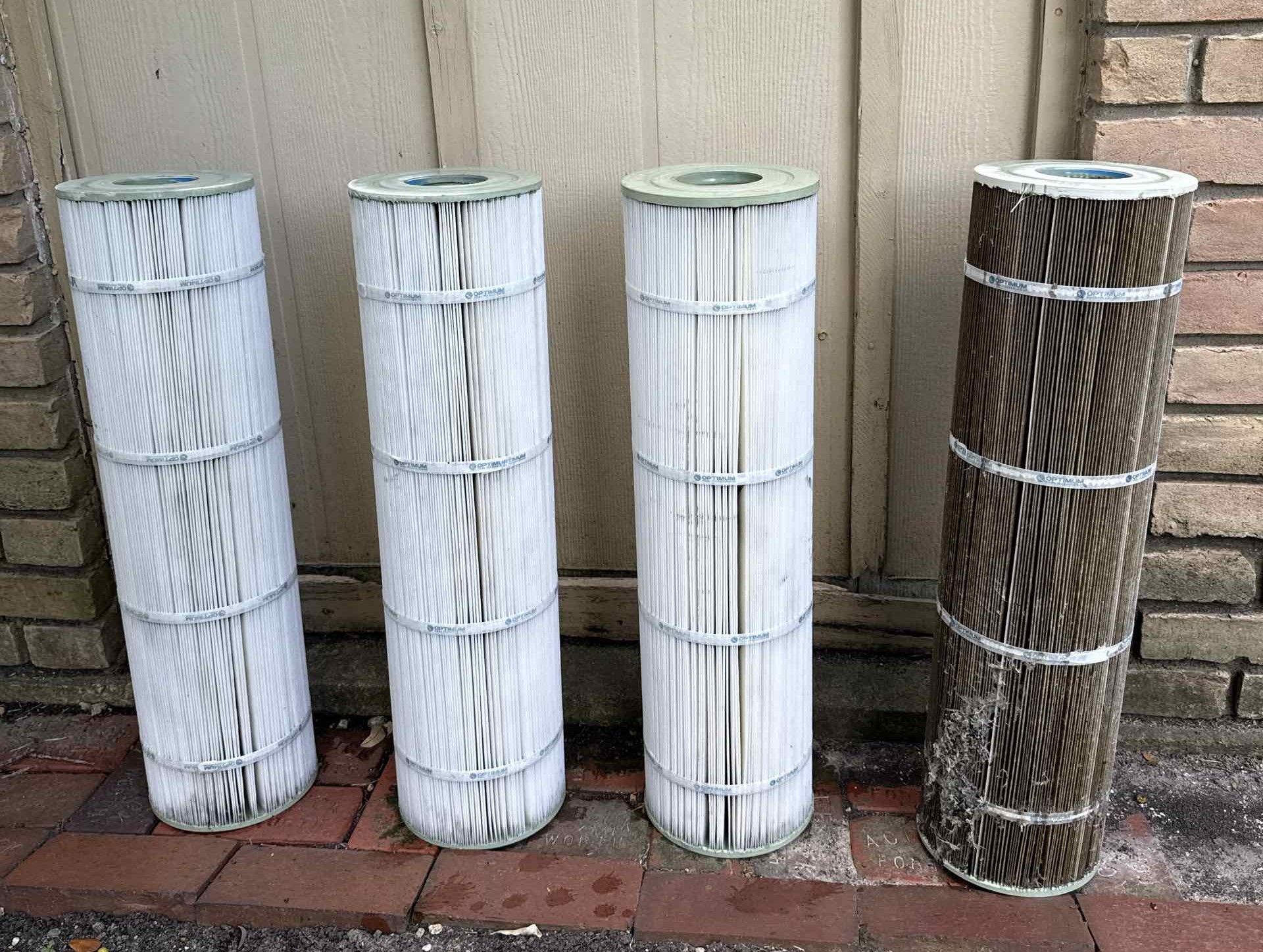 Two cylindrical air filters on grass, one with legs and a stick, the other lying down, against a wooden fence.