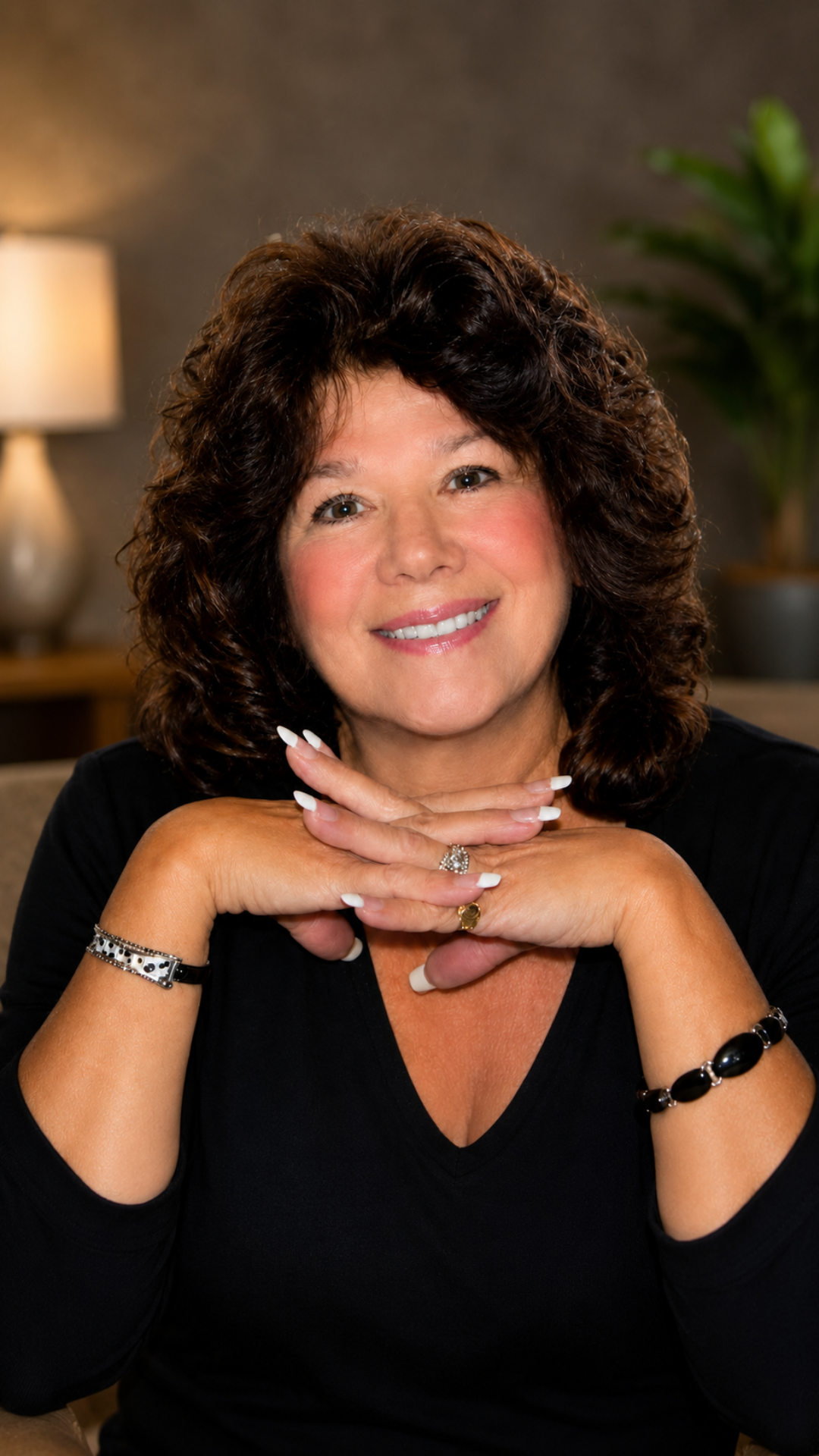 Smiling person in a black top, resting chin on hands in a warmly lit indoor setting