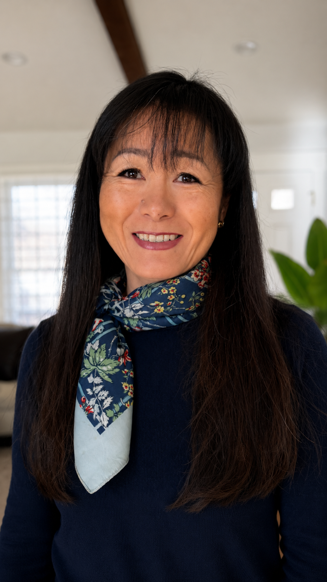 Smiling woman with long dark hair wearing a navy sweater and patterned scarf indoors