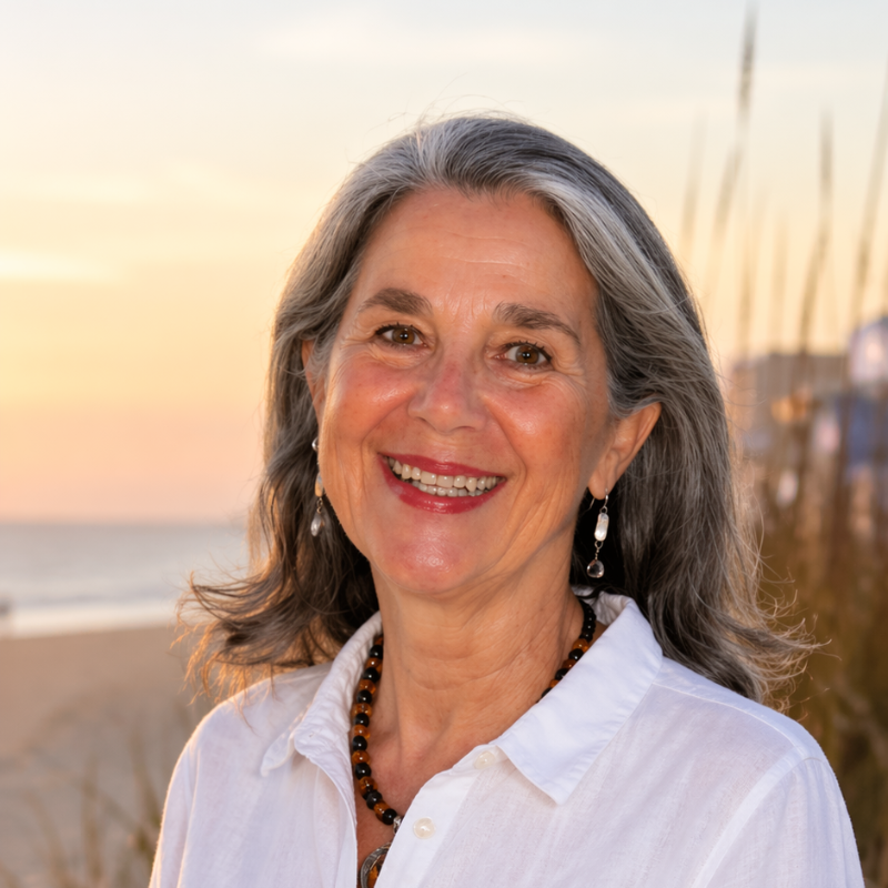 Smiling woman in a white shirt standing on a beach at sunset with tall grasses in the background