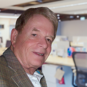 Smiling older man in a brown plaid jacket, white shirt, and light brown hair.
