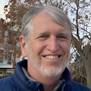 Smiling person in a navy jacket outdoors with trees in the background