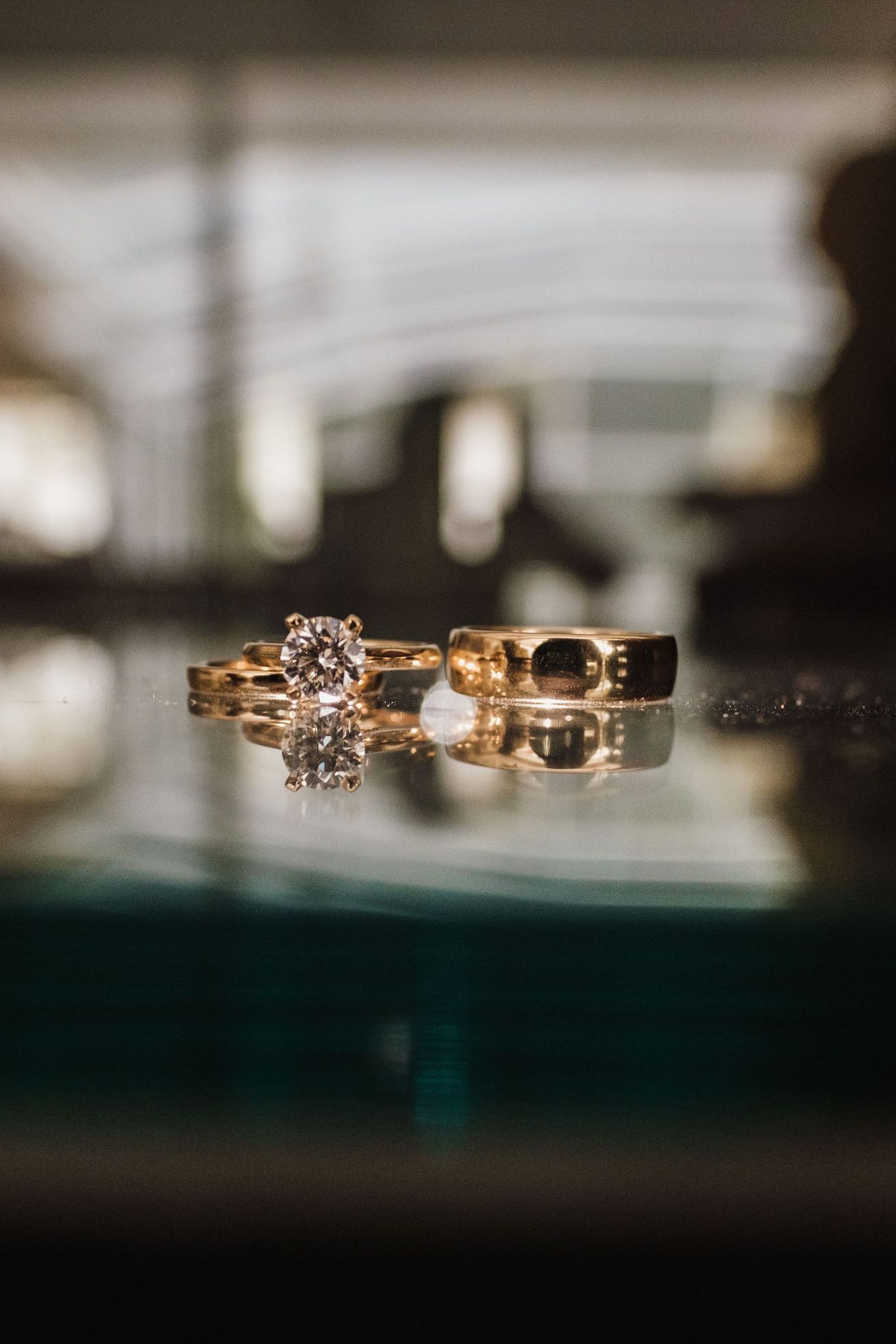 Anillos de oro con un diamante sobre una superficie reflectante y un fondo suavemente desenfocado