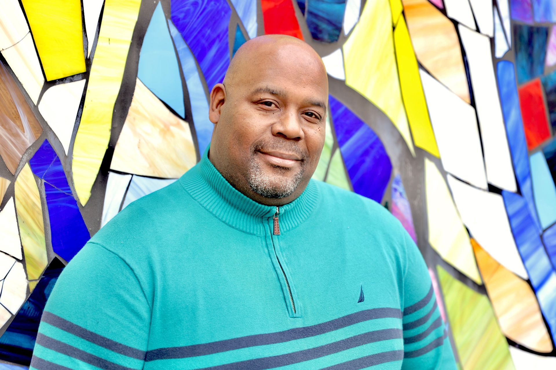 A man in a blue sweater is standing in front of a stained glass window.