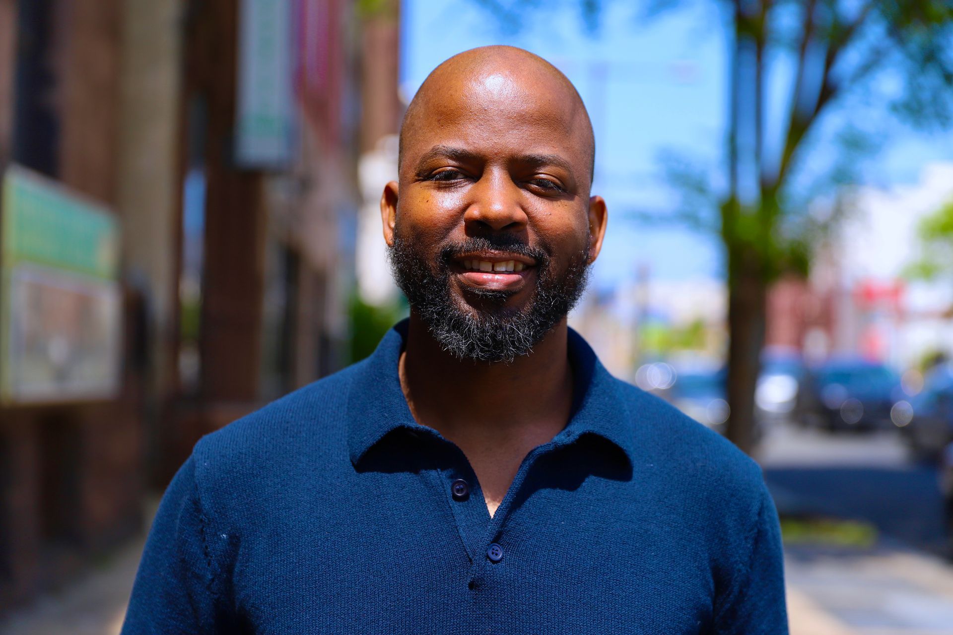 A man with a beard is wearing a blue shirt and smiling for the camera.