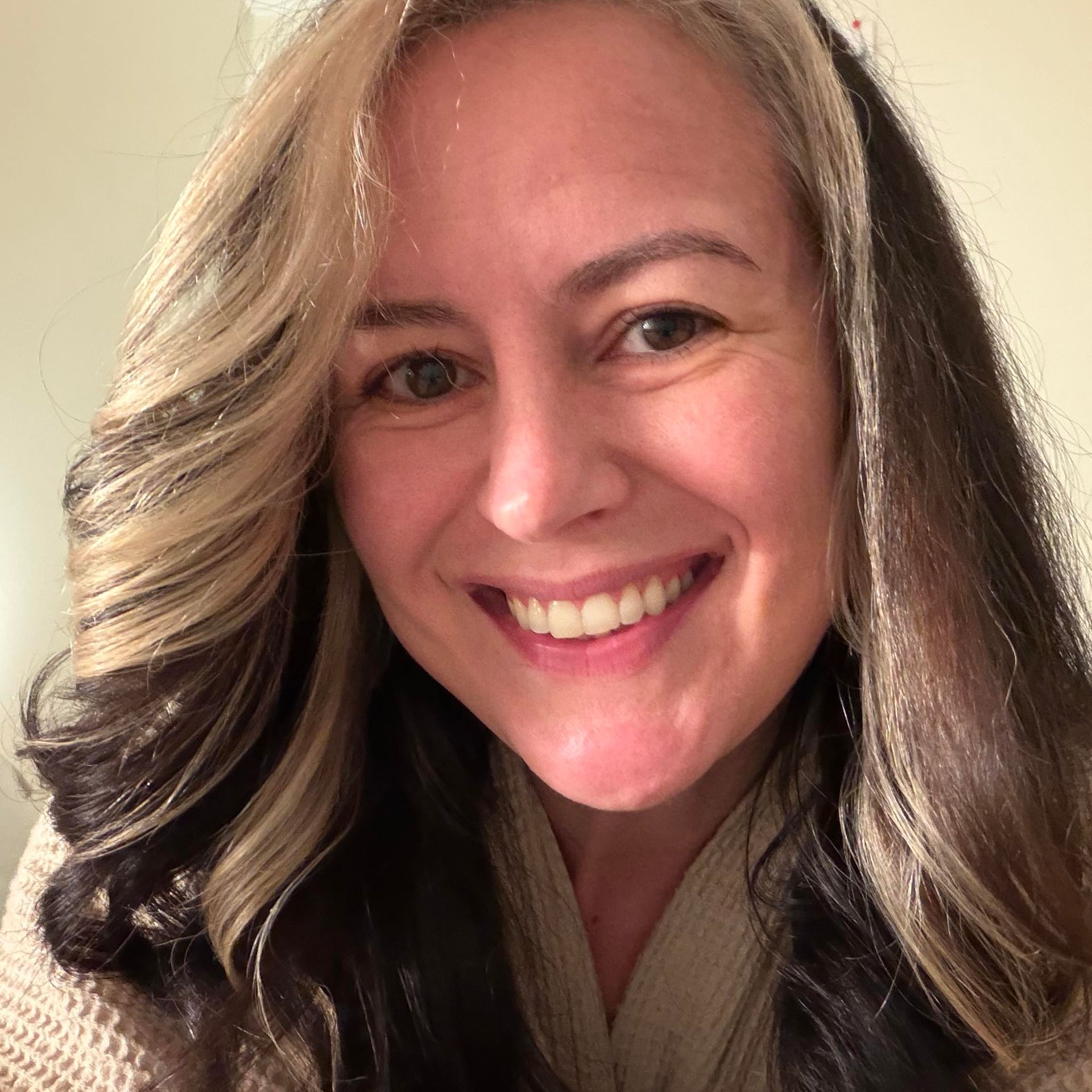 A smiling person with layered, shoulder-length brown hair featuring prominent blonde highlights.