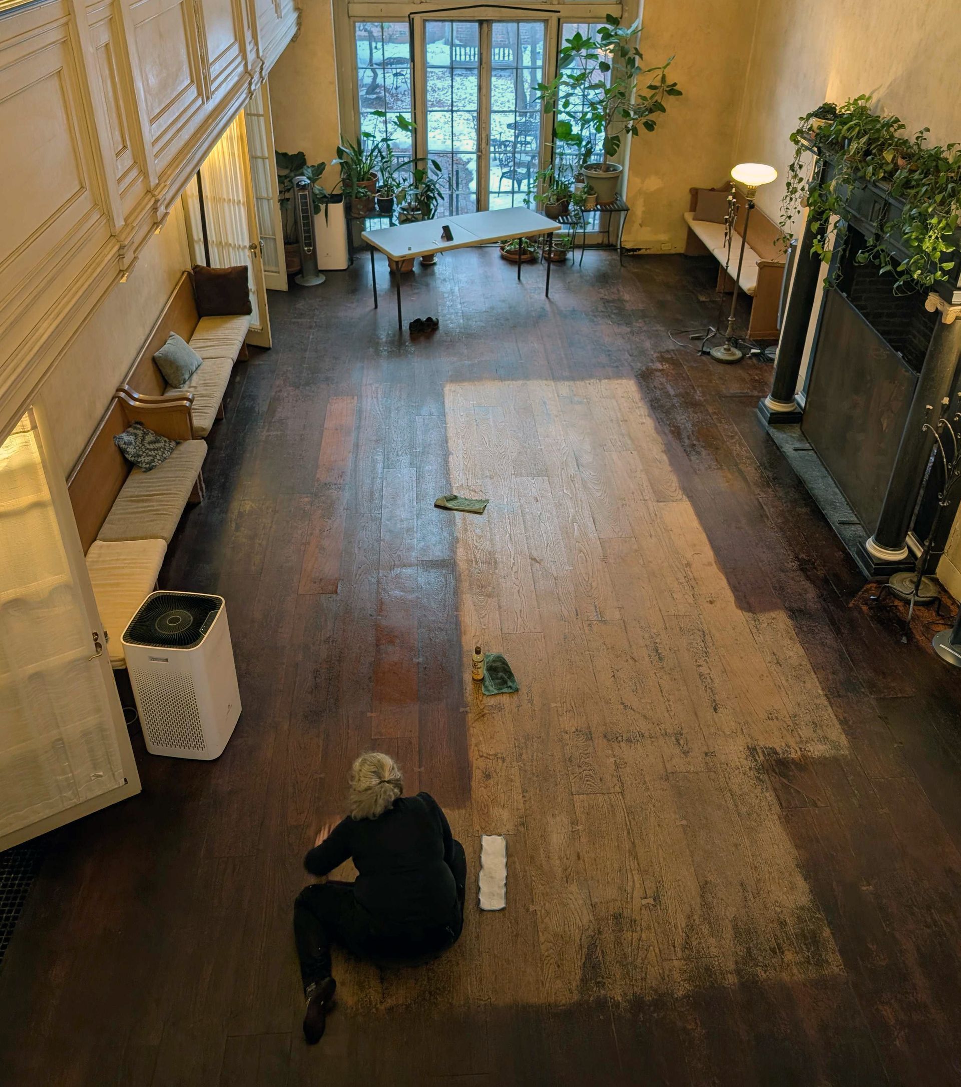 A woman sits on a large floor, most of which has been stained, but a patch remains unfinished.
