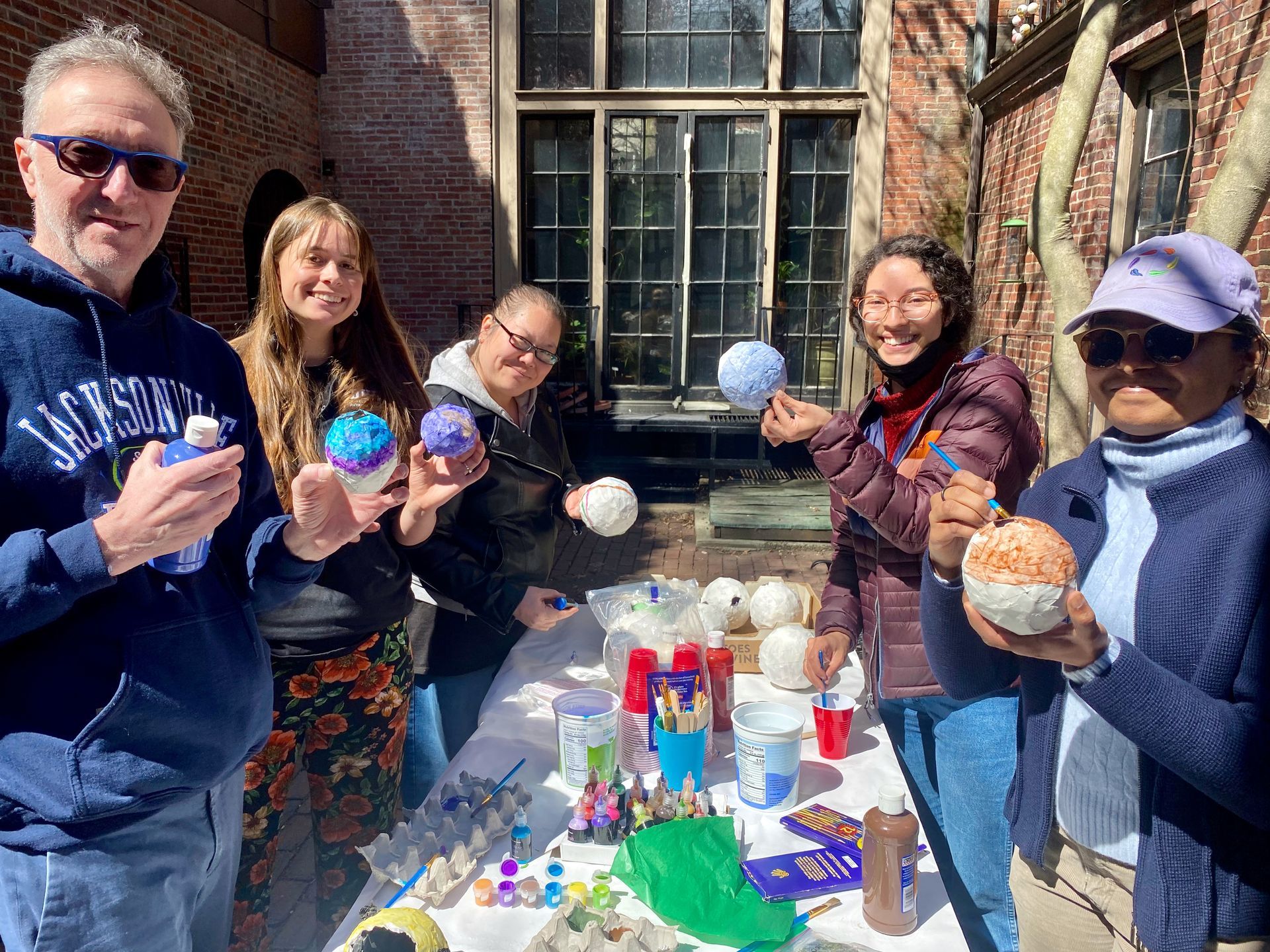 A group of BHFH residents standing around a table outdoors, holding and painting decorative spheres.